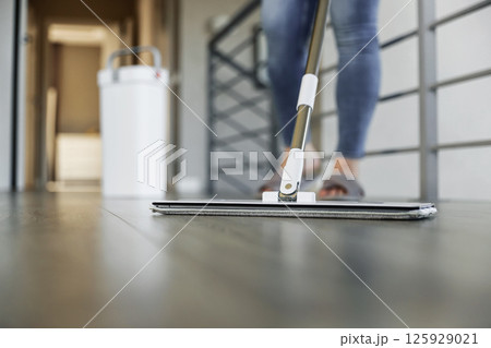 Woman mopping, wiping sleek hardwood floor in modern home setting. Housewife use cleaning mop in cozy living house room. Housekeeping, housework. Sanitation, cleanliness, hygiene, cleanup, maintenance 125929021