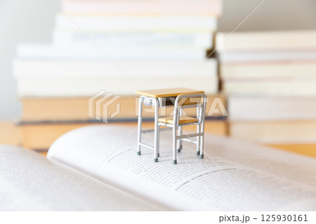 机の上に開いた英語の書籍とミニチュアの学校机  研究 学習のイメージ 125930161