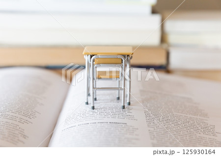 机の上に開いた英語の書籍とミニチュアの学校机  研究 学習のイメージ 125930164