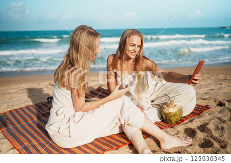 Cheerful Women Taking Selfies with Coconut Drinks on a Beach 125930345