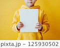 Child in yellow hoodie holding blank book against yellow background. Cover book Mockup 125930502