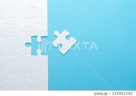 Concept for problem-solving, teamwork, solutions, or missing connections. White jigsaw puzzle on a vibrant blue background with one missing piece. Minimalist composition with copy space. 125932292