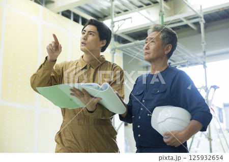 現場で図面を見ながら打ち合わせする現場監督  125932654