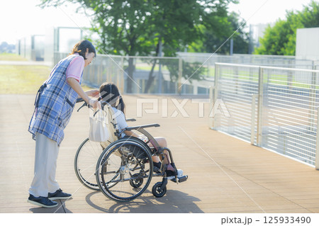 小学生が乗った車椅子を押す介護士 125933490