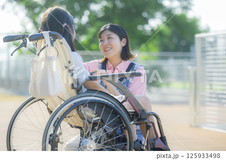 小学生が乗った車椅子を押す介護士 125933498