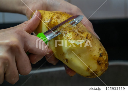Potapo peeling. Hands peeling raw potato with vegetable peeler in the kitchen.	 125933539