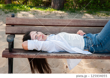 Young caucasian female in casual attire relaxing on a wooden bench at a sandy beach on a sunny day with nature in the background. Digital nomad lifestyle. Remote work 125934055