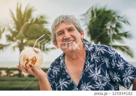 happy elderly male tourist holds a drinking coconut with a straw on vacation on a beach by the sea in the tropics 125934182