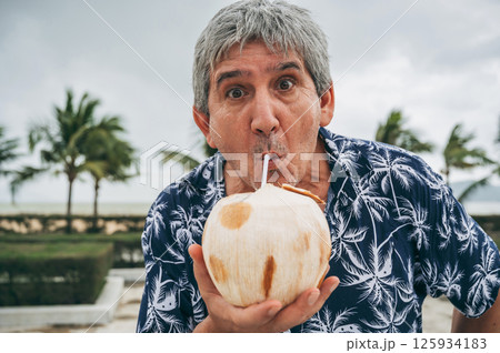 funny elderly male tourist drinks a drinking coconut with a straw on vacation on the beach by the sea in the tropics 125934183