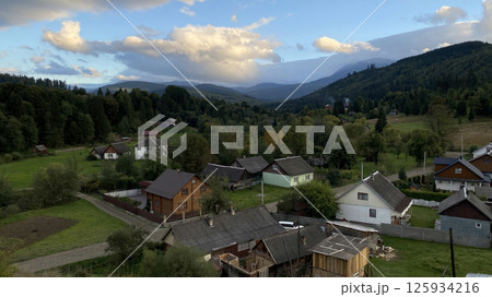 Scenic mountain village in Ukraine surrounded by lush forests and rolling hills during early evening. 125934216