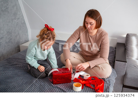 Top view of mother and daughter together packing a Valentine's Day and Mother's day gift. Caucasian woman and a little girl are preparing for the holiday Top view of mother and daughter together packing a Valentine's Day and Mother's day gift. Caucasian woman and a little girl are preparing for the holiday 125934374