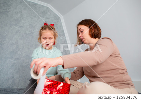 Bottom view of Caucasian mother and little cute daughter pack a holiday gift together. Woman teaches a child holiday preparation. Family celebration of Mother's Day 125934376