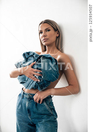 Model poses with denim clothing in a minimalist indoor setting during a fashion shoot 125934507