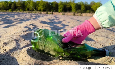 Closeup of volunteer hand in pink gloves putting plastic bottle inside plastic bag on the sand. A volunteer picks up a plastic bottle on the beach. Closeup of volunteer hand in pink gloves putting plastic bottle inside plastic bag on the sand. A volunteer picks up a plastic bottle on the beach. 125934691