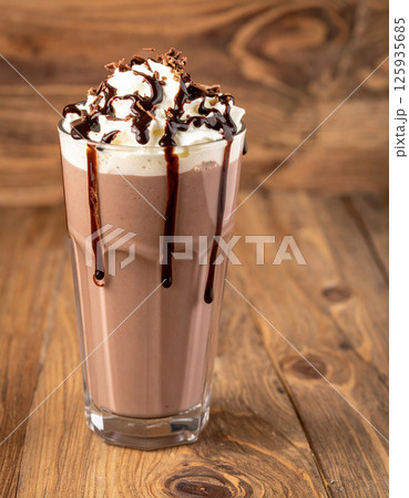 Creamy chocolate milkshake topped with whipped cream and chocolate syrup on wooden table 125935685