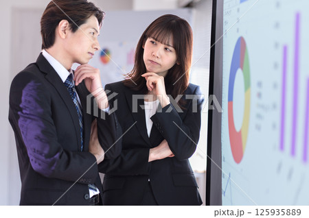 プレゼン内容に悩むスーツ姿の若い男女 プレゼン内容に悩むスーツ姿の若い男女 125935889