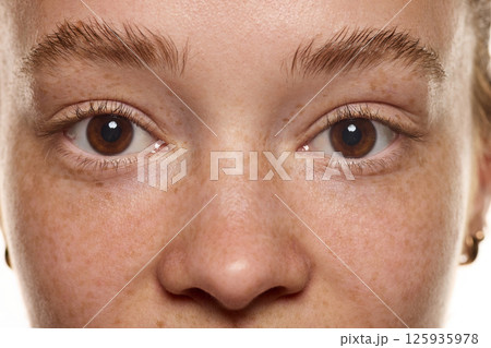 Close-up of woman face with freckles, without makeup, brown eyes, nose and well groomed eyebrows. Beauty of natural skin textures Close-up of woman face with freckles, without makeup, brown eyes, nose and well groomed eyebrows. Beauty of natural skin textures 125935978