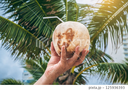 drinking coconut with a straw in a man's hand on background of palm trees. Concept of traveling and relaxing in a tropical resort on a sunny day drinking coconut with a straw in a man's hand on background of palm trees. Concept of traveling and relaxing in a tropical resort on a sunny day 125936393