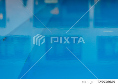 Close up out of focus bright blue water of indoor swimming pool with houseplants and large panoramic windows, lighting. Interior part of luxury modern wellness spa hotel. Healthy concept. 125936689