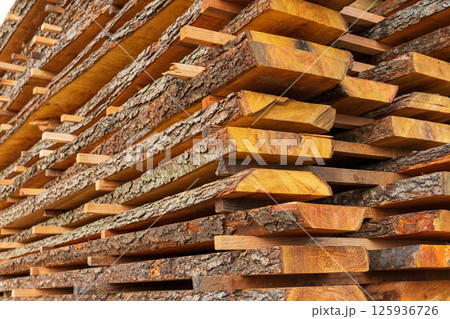 Wooden planks are neatly stacked and drying in the sunlight at a lumber yard, showcasing the natural textures and colors of the wood 125936726