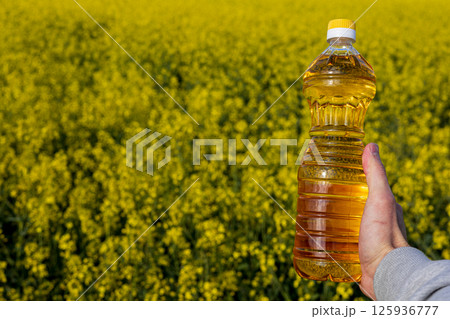 A person holds a bottle of golden canola oil in front of a vast field of bright yellow rapeseed flowers, showcasing nature's bounty 125936777