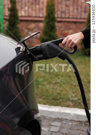 Unrecognisable woman inserting EV charger plug from public or home charging station for modern electric or hybrid car at special place for e-car. Concept eco-friendly sustainability energy car 125936850