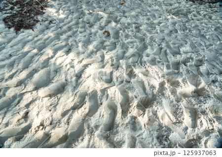 Close-up texture of soft white coral sand with footprints, lit by tropical sunlight on a beach Close-up texture of soft white coral sand with footprints, lit by tropical sunlight on a beach 125937063