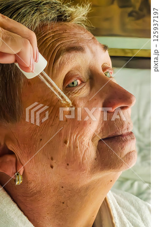 Elderly woman uses dropper to apply serum on her face in bright room. High quality photo Elderly woman uses dropper to apply serum on her face in bright room. High quality photo 125937197