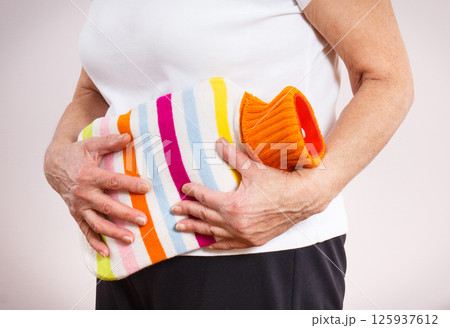 Senior woman with hot water bottle on her stomach. Help with pain in old age Senior woman with hot water bottle on her stomach. Help with pain in old age 125937612