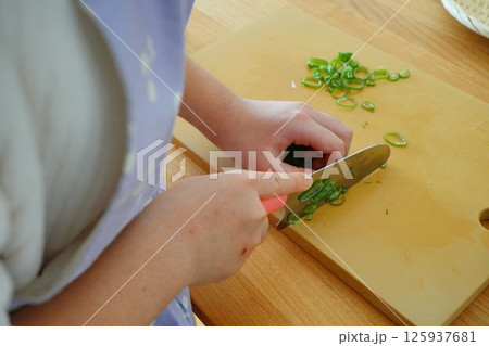 小学生5年生のの子供が包丁でネギを切っている手元 125937681