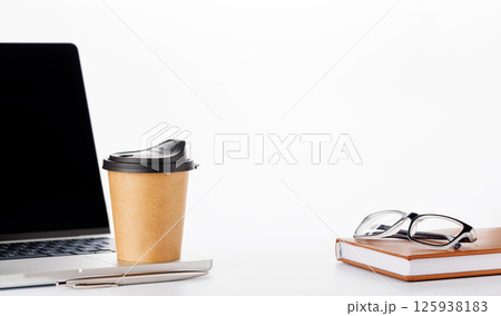 Closeup of an office table featuring a sleek laptop, a coffee cup, and reading glasses on a clean white surface Closeup of an office table featuring a sleek laptop, a coffee cup, and reading glasses on a clean white surface 125938183