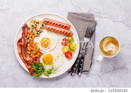 A classic breakfast plate featuring sunny-side-up eggs, crispy bacon, sausages, and fresh tomatoes A classic breakfast plate featuring sunny-side-up eggs, crispy bacon, sausages, and fresh tomatoes 125938185