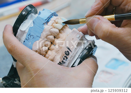 Dental Technician Carefully Brushes Denture Mold During Manufacturing 125939312