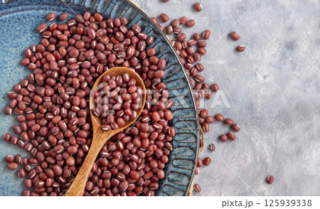 Blue plate full of dried red azuki beans with a wooden spoon top view. Vegetarian protein source 125939338
