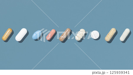 Medical capsules and pills in a line on blue top view, hard shadow. Medicine and healthcare Medical capsules and pills in a line on blue top view, hard shadow. Medicine and healthcare 125939341