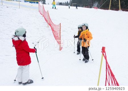Children enjoying skiing lessons in a snowy landscape, sharing excitement and learning on a winter day at a ski resort with a beautiful backdrop of trees 125940923