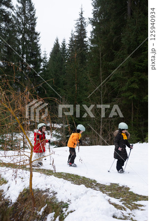 Children skiing through a snowy forest trail on a chilly winter afternoon, surrounded by tall evergreen trees and serene nature 125940934