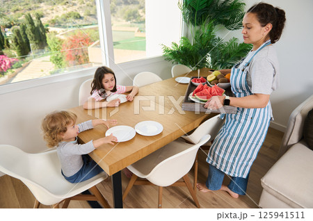 Mother Serving Healthy Breakfast to Children at Dining Table in Bright Home Mother Serving Healthy Breakfast to Children at Dining Table in Bright Home 125941511