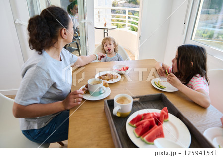 Mother and Children Enjoying a Family Breakfast in a Bright Kitchen Mother and Children Enjoying a Family Breakfast in a Bright Kitchen 125941531