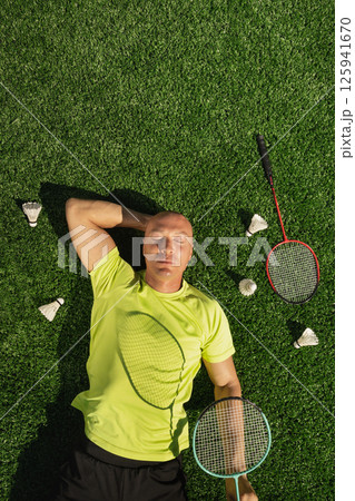 Badminton player resting after game, lying and enjoy on sport court in public park with artificial turf as green grass. Outdoors. Creative. Summer relax. View from above Badminton player resting after game, lying and enjoy on sport court in public park with artificial turf as green grass. Outdoors. Creative. Summer relax. View from above 125941670