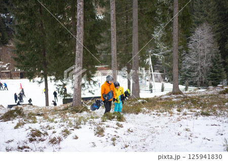 Families enjoying a winter day at the ski resort with children learning to snowboard under the trees on a snowy slope during midday Families enjoying a winter day at the ski resort with children learning to snowboard under the trees on a snowy slope during midday 125941830