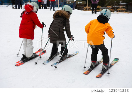 Joyful children ski downhill on a snowy slope at a winter resort, demonstrating excitement and camaraderie during a day of learning and fun in the crisp mountain air Joyful children ski downhill on a snowy slope at a winter resort, demonstrating excitement and camaraderie during a day of learning and fun in the crisp mountain air 125941838