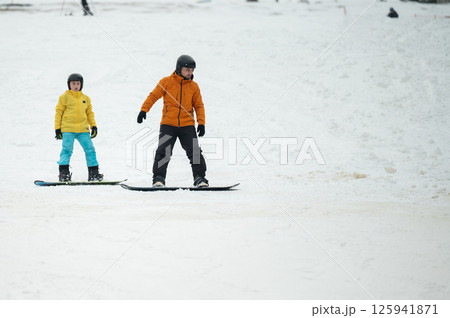Snowboarding adventure unfolds on a wintery slope as a child and adult embrace the thrill of the snowy landscape together Snowboarding adventure unfolds on a wintery slope as a child and adult embrace the thrill of the snowy landscape together 125941871