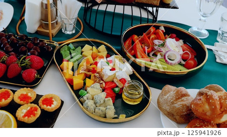 Abundant catering platters displaying colorful cheeses, crisp vegetables, ripe fruits, and freshly baked bread presenting elegant buffet centerpiece 125941926