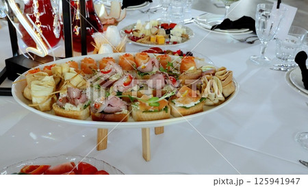 Gourmet bite sized sandwiches and salmon canapes garnished with red caviar, artfully plated on pristine white oval surface, highlighting elegant appetizer presentation 125941947