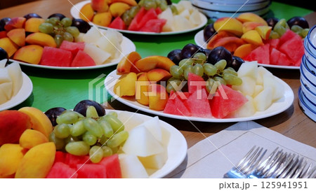 Fresh fruit plates featuring watermelon, peaches, grapes, and melon displayed on catering table, presenting vibrant, nutritious dessert selection for guests Fresh fruit plates featuring watermelon, peaches, grapes, and melon displayed on catering table, presenting vibrant, nutritious dessert selection for guests 125941951