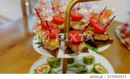 Small snacks on skewers with tomatoes and meat on rye bread are waiting for guests at a banquet, catering service offers delicious canapes 125942011