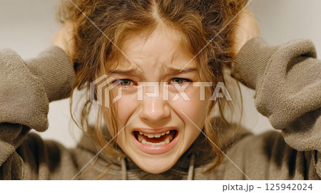 A young girl holds her head and screams loudly in fear 125942024