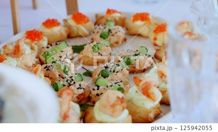 Gourmet catering presenting elegant seafood canapes topped with shrimp, cucumber, red caviar, garnished with black sesame seeds at festive gatherings Gourmet catering presenting elegant seafood canapes topped with shrimp, cucumber, red caviar, garnished with black sesame seeds at festive gatherings 125942055