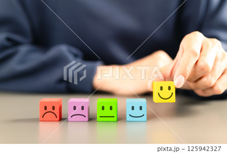 Customer satisfaction feedback survey concept. Person selects yellow smile face block from row of colorful blocks various facial expressions, different levels of customer satisfaction, feedback rating 125942327